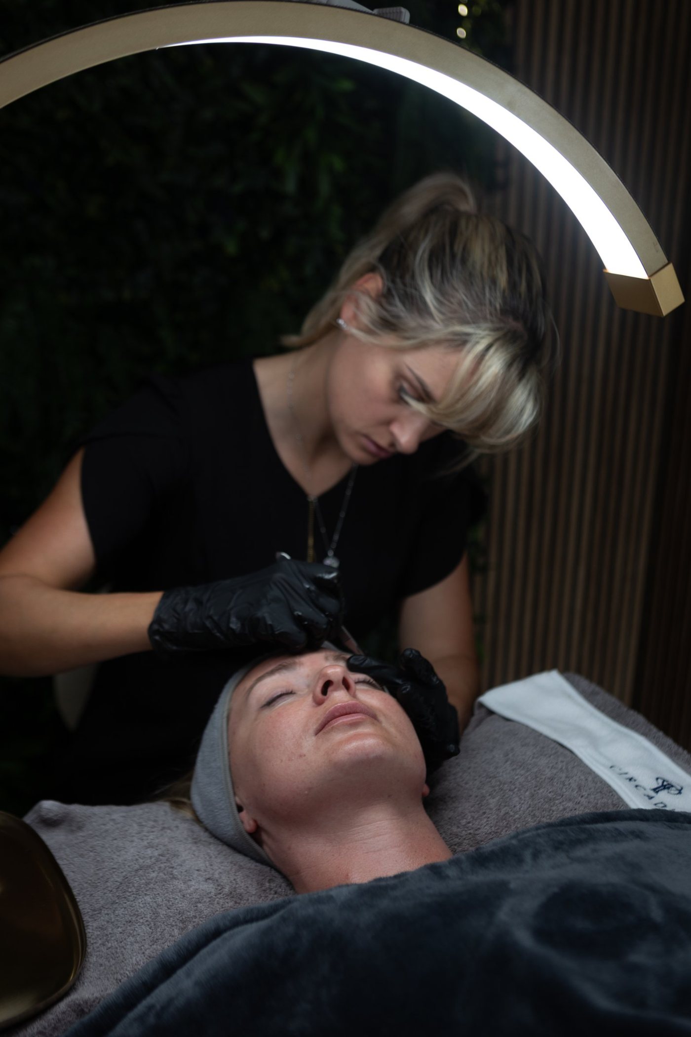 Sarah performing a facial under the arch lamp in front of the green wall