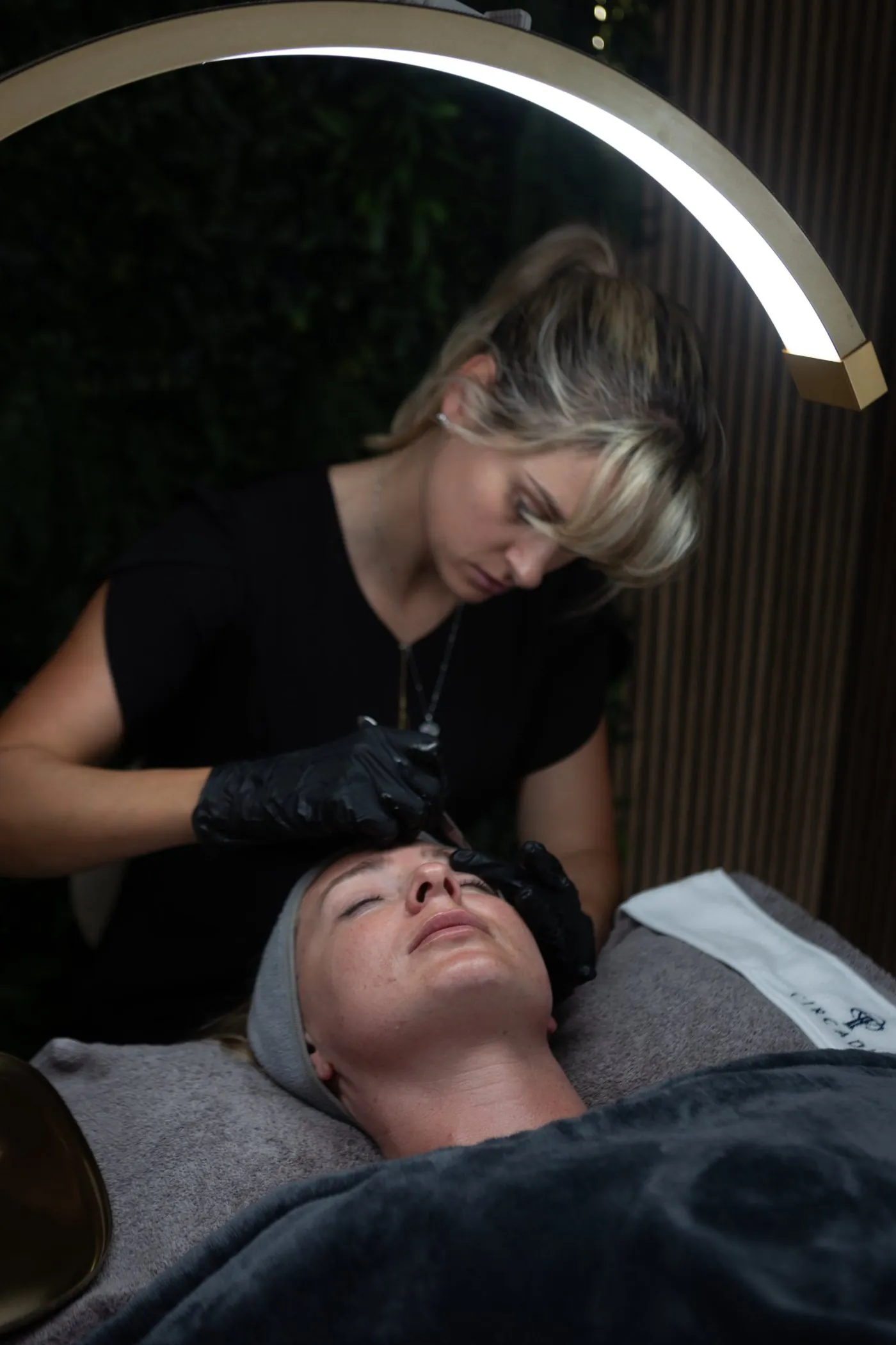 Sarah performing a facial under the arch lamp in front of the green wall
